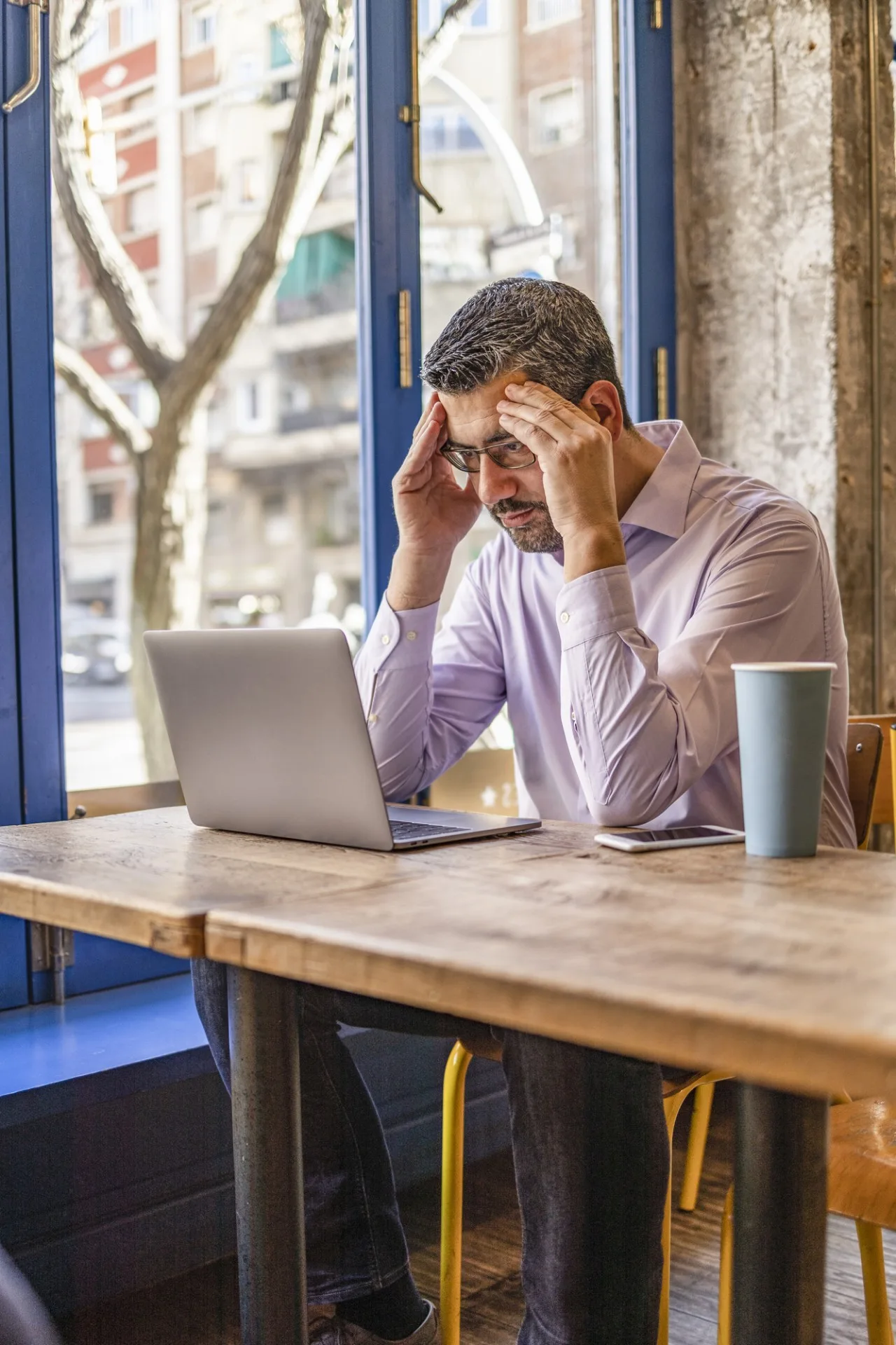 photo of a frustrated and overwhelmed small business owner in a coffee shop reviewing his financial statements, struggling to get ahead and stay organized